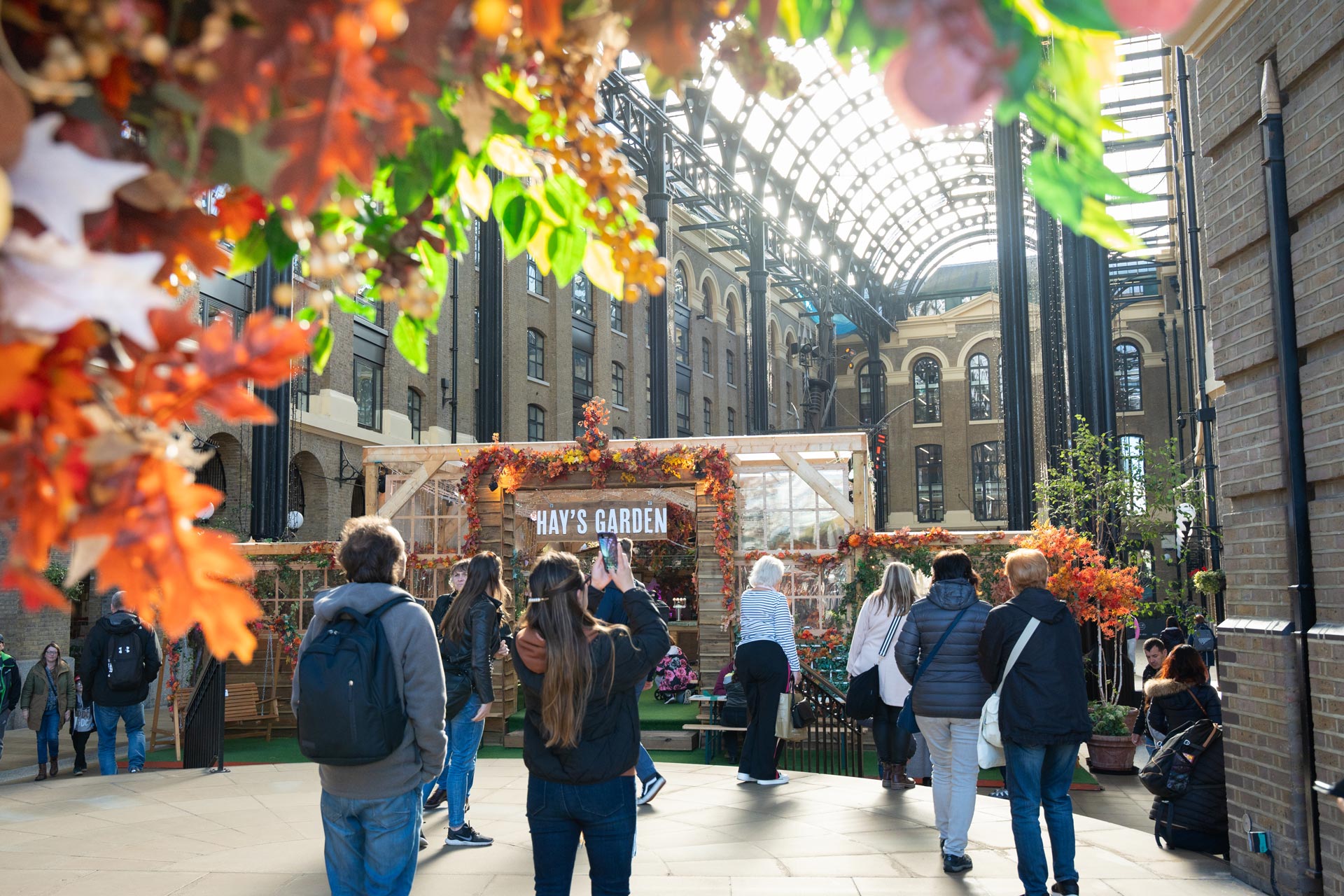 Visitors walking through Hay's Galleria at London Bridge, decorated with autumn foliage and a Hay's Garden display.